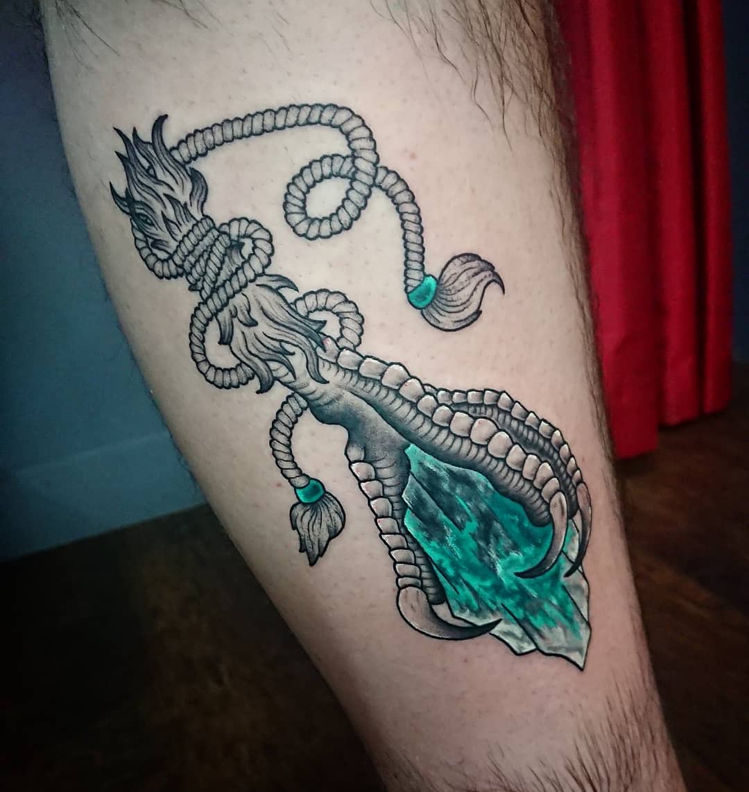 Tattoo of a gemstone dagger with a decorative handle and rope on the back of their leg